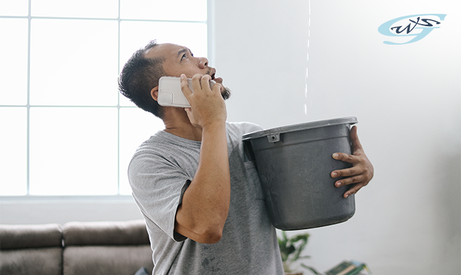 A man holding a bucket to catch water leaking from the roof while calling for help