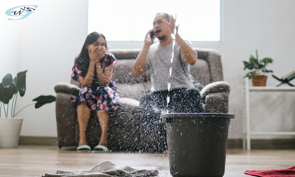 Water leaking from the roof into a bucket in the living room in front of a couple