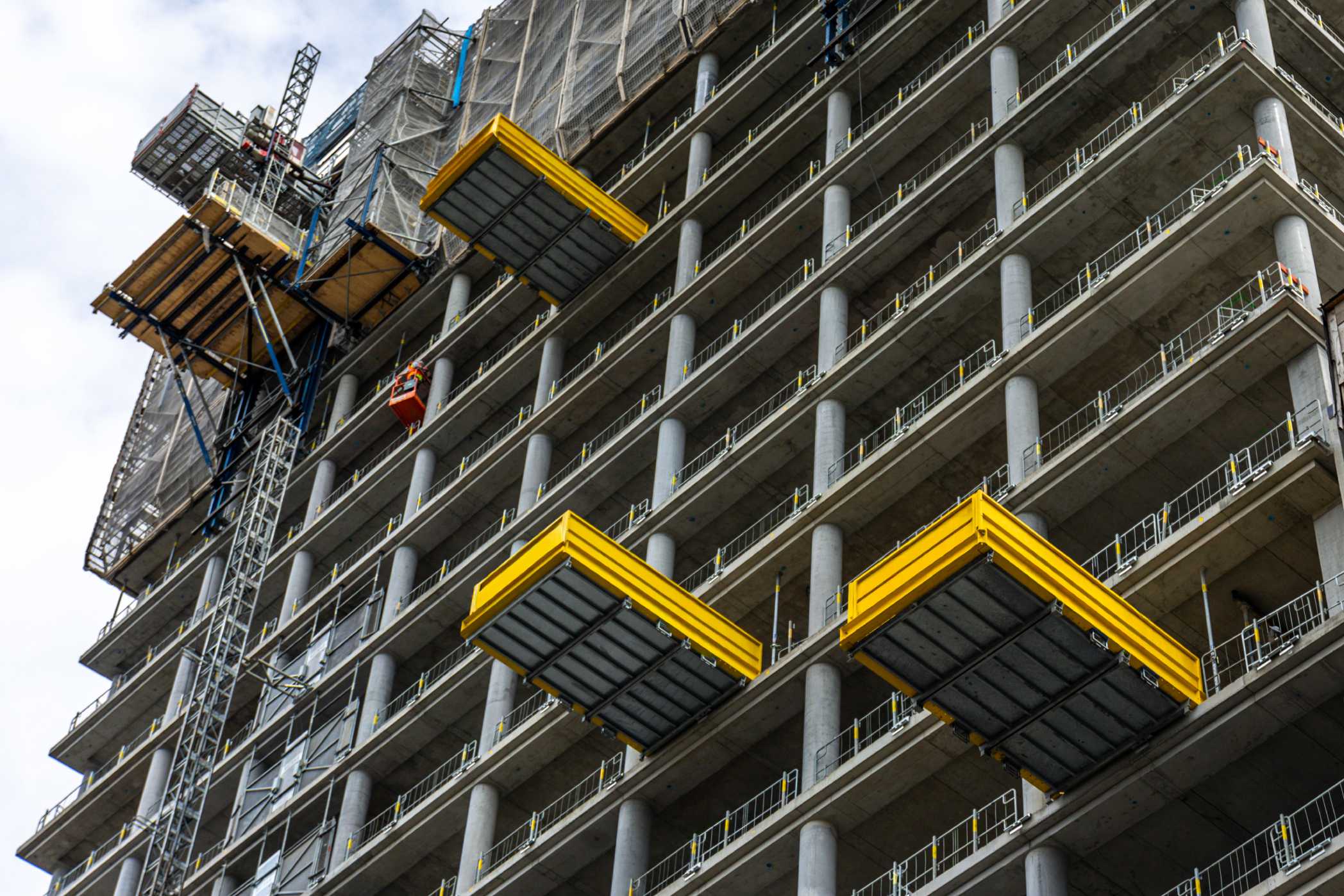 A high-rise building under construction with yellow loading platforms