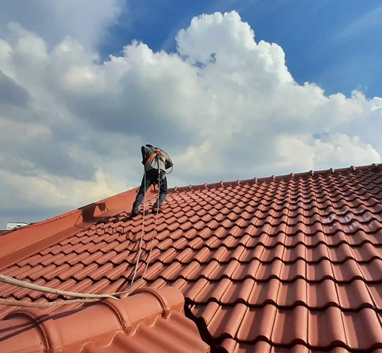 Harnessed worker performing waterproofing on a pitched tiled roof