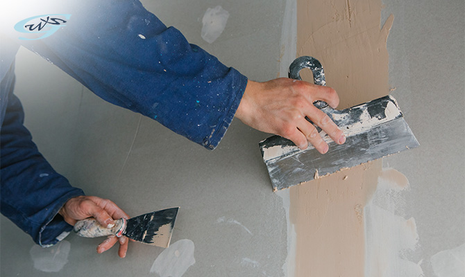 Worker applying joint compound to repair a drywall seam.